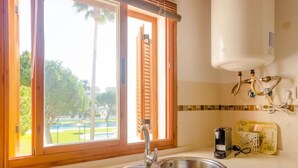 A kitchen with a double sink, a window with a view of greenery, and a water heater mounted on the wall.
