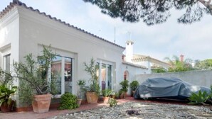 A white building with a tiled roof, a covered car, and potted plants in a garden area. - Villa The Beach 14882 (Chiclana de la Frontera)