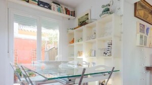 A dining area with a glass-top table and four chairs, surrounded by white shelving units filled with books and decorative items. - Villa The Beach 14882 (Chiclana de la Frontera)