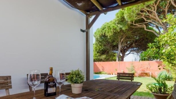 An outdoor wooden table with a newspaper, two wine glasses, and a bottle of liquor. - Villa The Beach 14882 (Chiclana de la Frontera)
