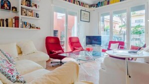 A living room with a white sofa, red chairs, a glass coffee table, and a bookshelf filled with books. - Villa The Beach 14882 (Chiclana de la Frontera)