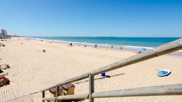 A beach with a wooden walkway leading to the shore, a clear blue sky, and a calm sea. - Duplex El Manantial 16345 (El Puerto de Santa Maria)