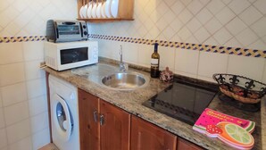 Una cocina con microondas, tostadora, lavamanos, una botella de vino y una cesta de frutas.