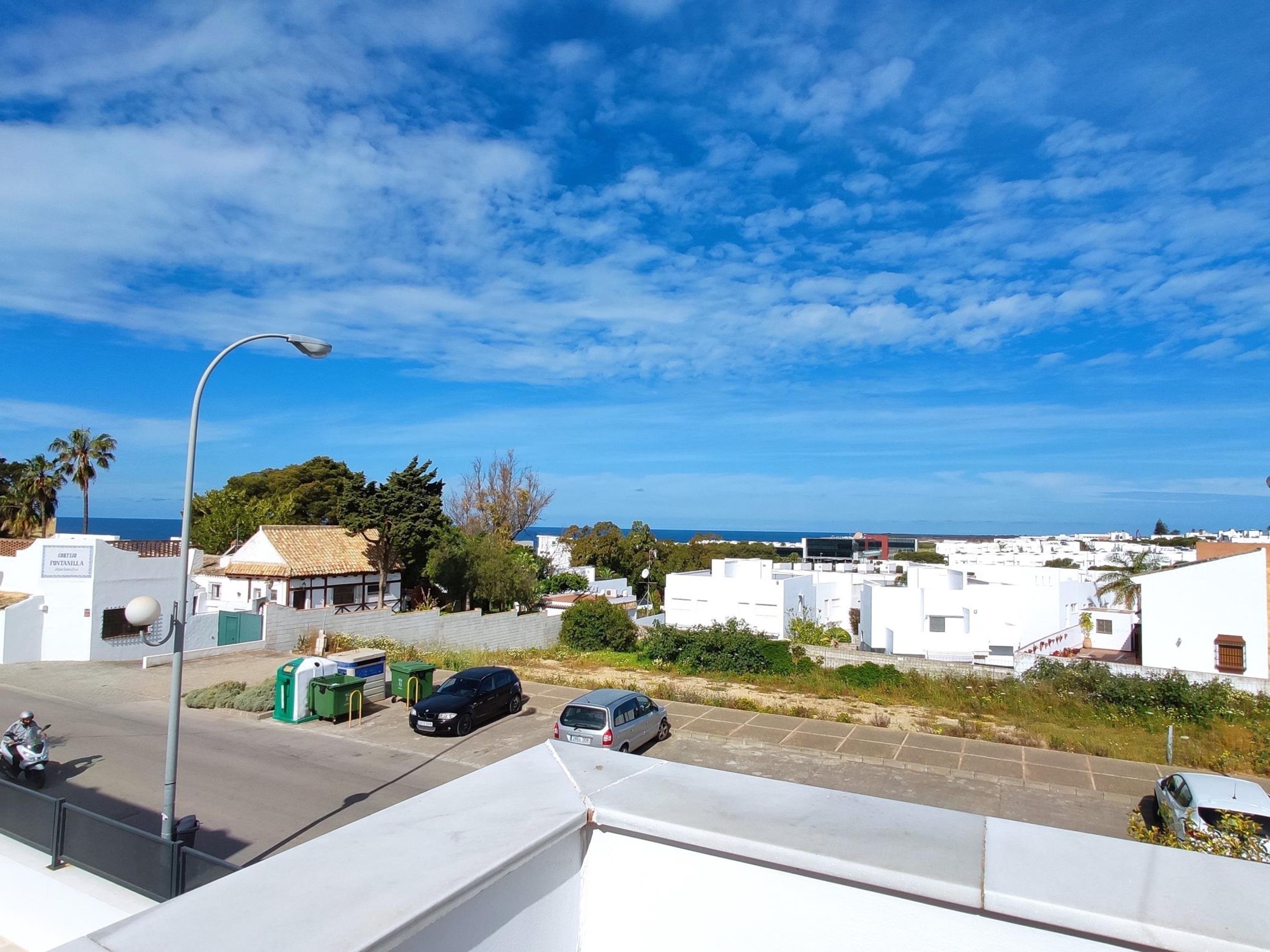 A coastal residential area with white houses, a street with parked cars, and a clear blue sky.