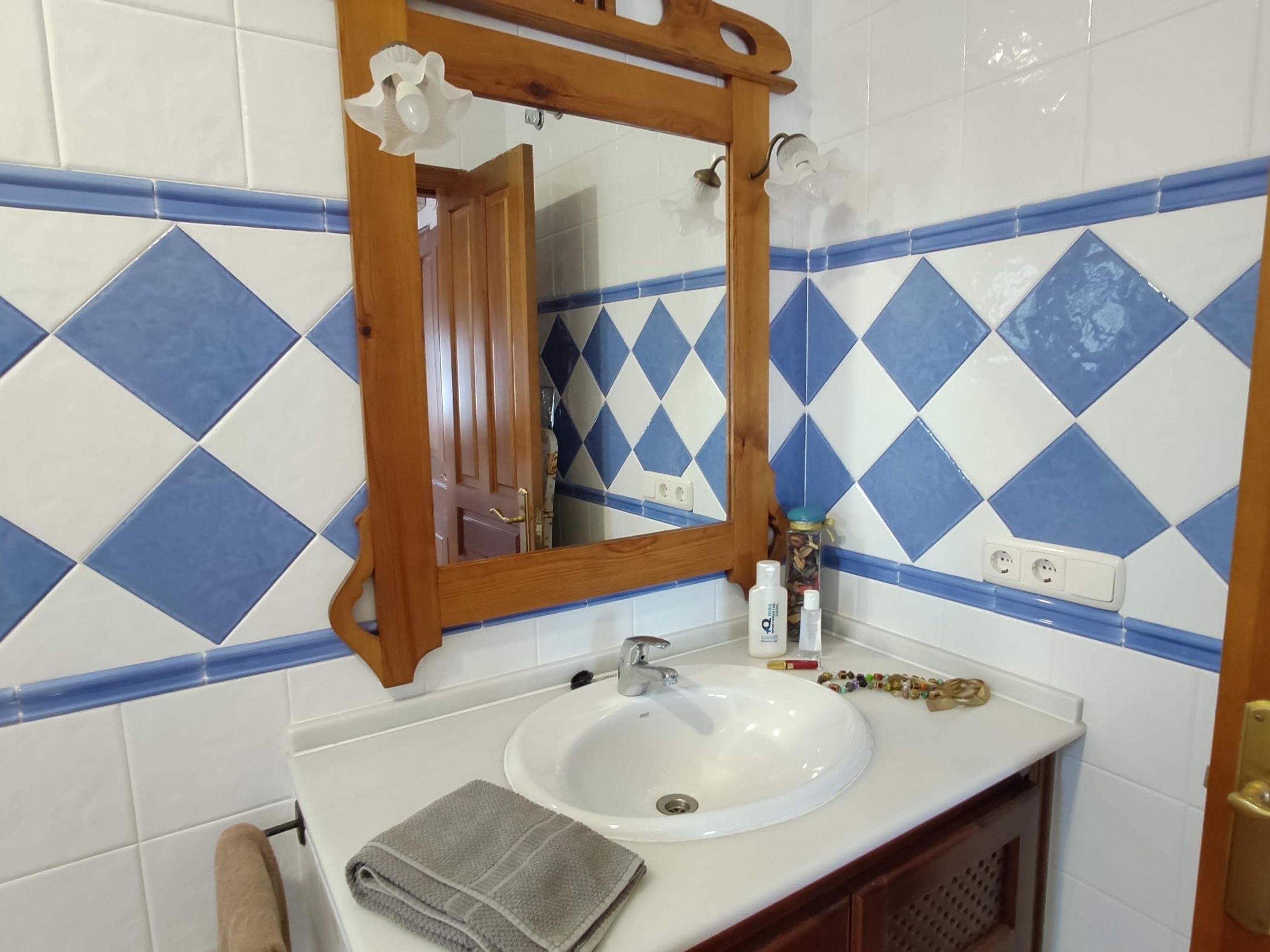 A bathroom with a white sink, a mirror, and blue and white diamond-patterned tiles.