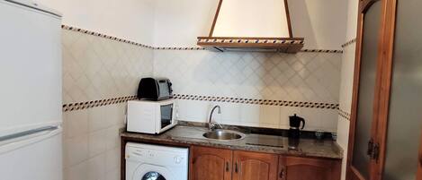 A compact kitchen with a washing machine, a microwave, a sink, and wooden cabinets.