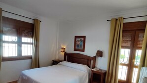 A hotel room with a bed, a nightstand, a wall-mounted lamp, and a painting. - Rezon 1 5012 in Conil de la Frontera (Conil de la Frontera)