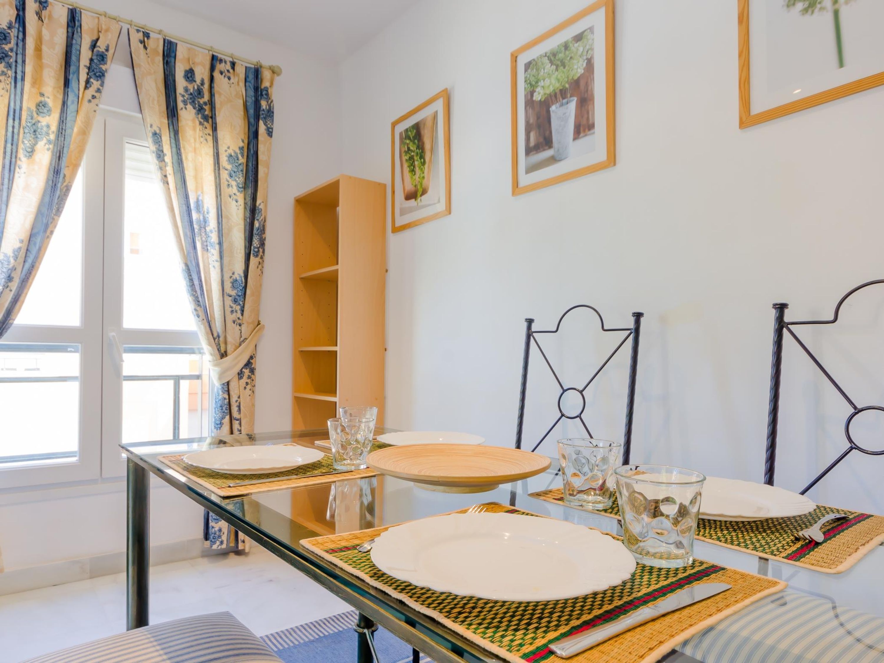 A dining area with a glass table set for four, a wooden sideboard, and two metal chairs.