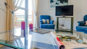 A living room with a glass table, two blue armchairs, a flat-screen TV, and a painting of a coastal scene. - 13329 Ancora 10234 in El Puerto de Santa Mar a (El Puerto de Santa Maria)