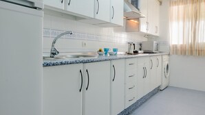 A modern kitchen with white cabinets, a granite countertop, and a built-in washing machine. - Apartamento La Capillita de Sanl car 15244 (Sanlucar de Barrameda)
