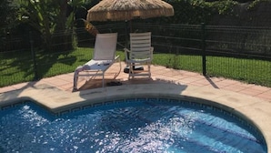 A swimming pool with two lounge chairs and a thatched umbrella. - Villa La Vega 14354 in Chiclana (Chiclana de la Frontera)