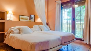 A double bed with white linens, a bedside table, a lamp, and a window with curtains. - Villa La Vega 14354 in Chiclana (Chiclana de la Frontera)