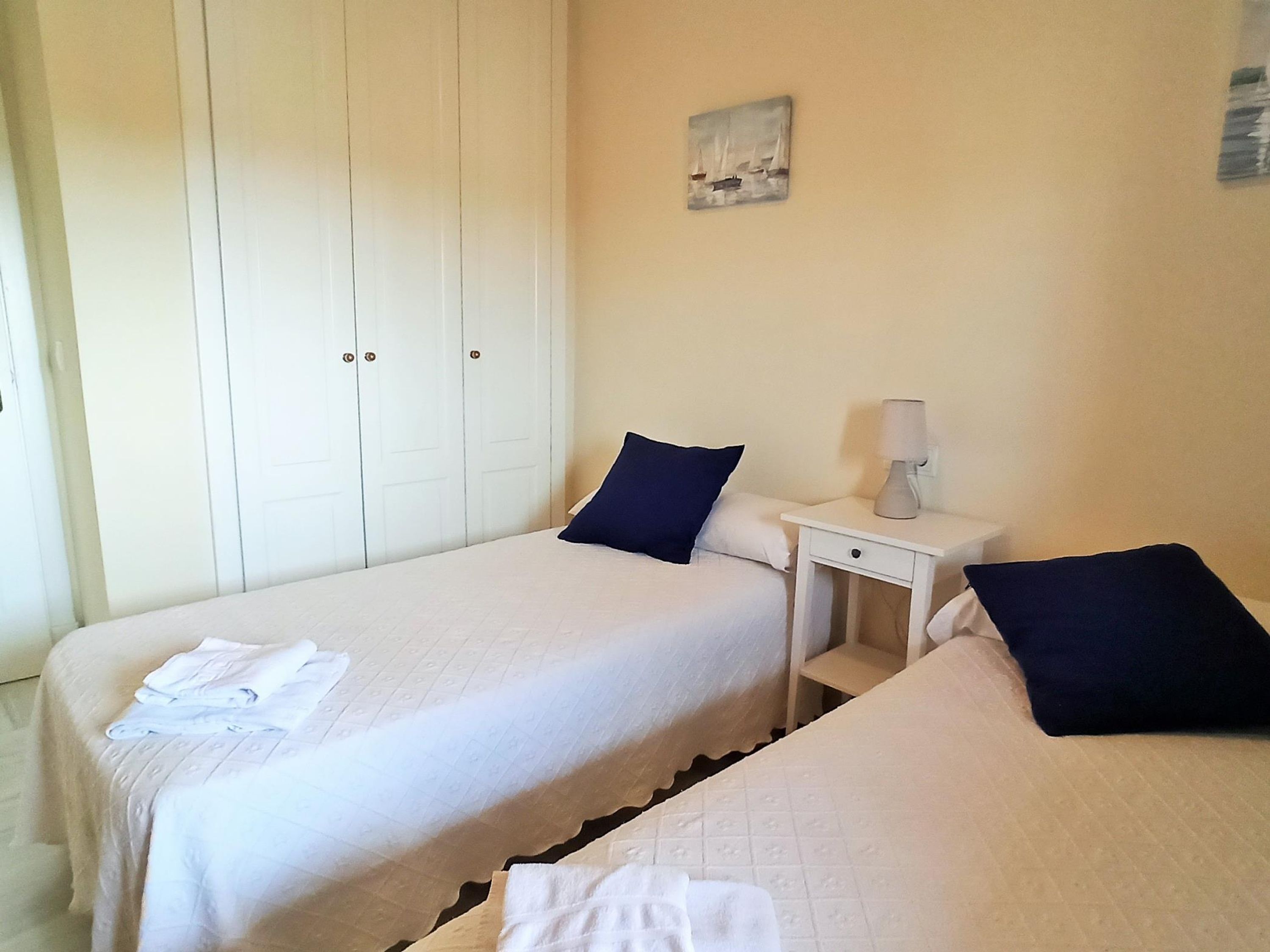 Ein Hotelzimmer mit zwei Betten, einem Kleiderschrank, einem Nachttisch mit Lampe und einem Bild an der Wand.