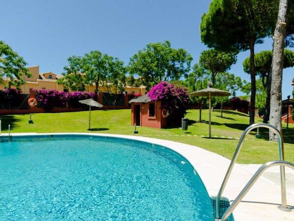 A swimming pool with clear blue water, surrounded by well-maintained grass and trees. - Dunas II 2D 15436 in El Puerto de Santa Mar a (El Puerto de Santa Maria)