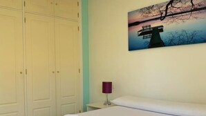 Una habitación de hotel con una cama, un cuadro de un faro y una mesita de noche con lámpara.