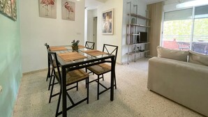 Una sala de estar moderna con una mesa de comedor de vidrio, sillas negras, un sofá beige y un televisor en un estante.