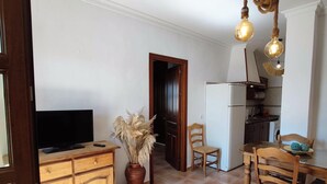A compact kitchen with a TV, wooden cabinets, a vase of dried plants, and a dining area with chairs and a table. - Rezon 3 5567 in Conil de la Frontera (Conil de la Frontera)