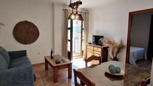 A living room with a sofa, a coffee table, a dining table with chairs, a TV on a cabinet, and a decorative wall hanging. - Rezon 3 5567 in Conil de la Frontera (Conil de la Frontera)