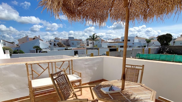 A rooftop terrace with a bamboo table and chairs, a thatched umbrella, and a view of white buildings in the background. - Rezon 3 5567 in Conil de la Frontera (Conil de la Frontera)