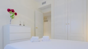 Una camera d'albergo con un letto grande, una cassettiera bianca e un vaso con fiori rossi.