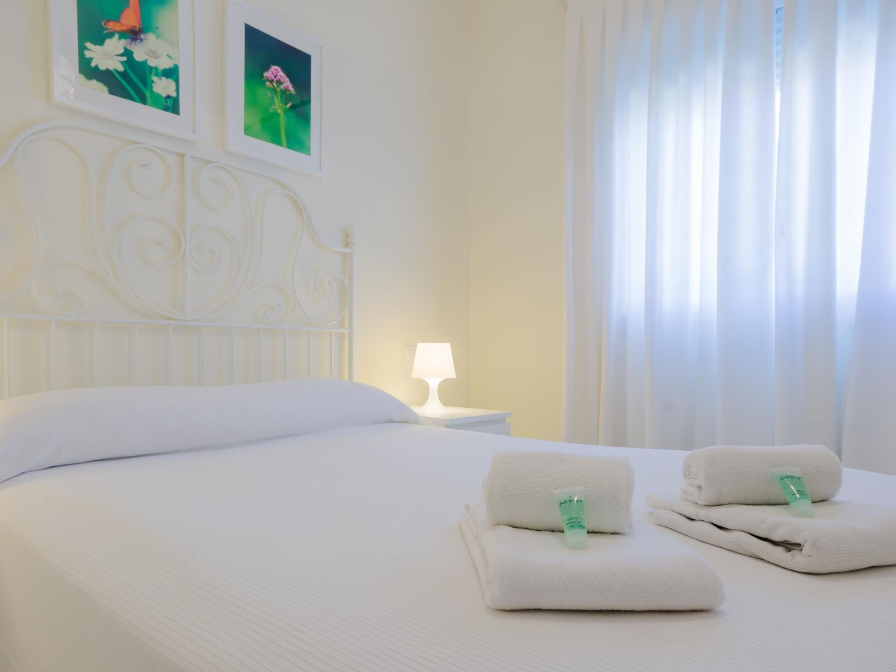Una camera d'albergo con un letto rifatto, una lampada da comodino e due asciugamani con una bottiglia verde sopra.