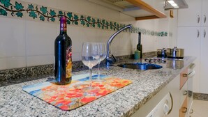 Una cucina con piano di lavoro in granito, una bottiglia di vino, due bicchieri da vino e una schiena di caminetto con motivo a foglia.
