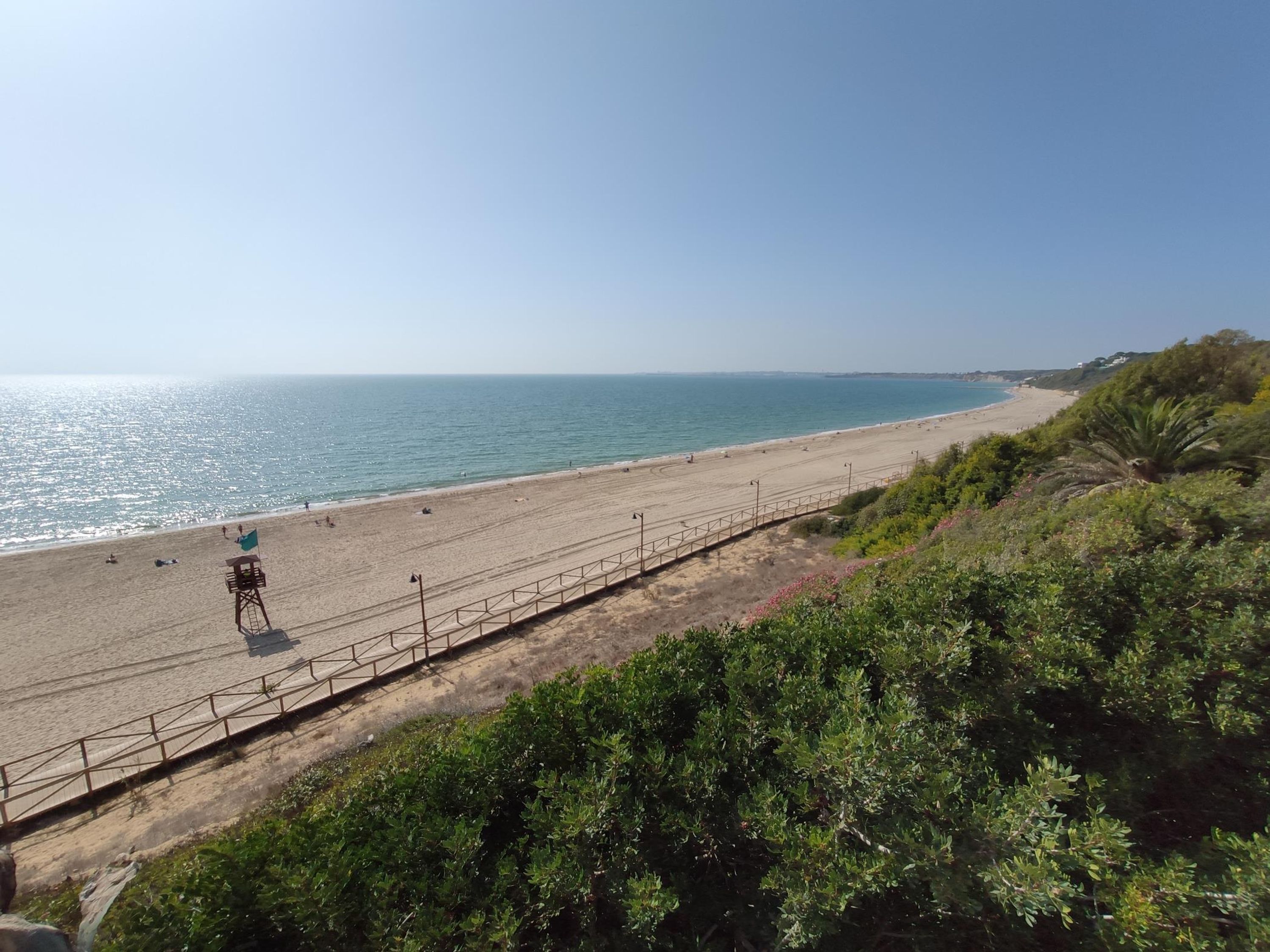 A beach with a lifeguard tower, a fence, and greenery.