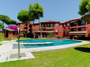 A swimming pool surrounded by a well-maintained lawn, with a red building in the background.