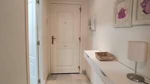 A hallway with a white door, a small table with a lamp, and framed artwork on the wall.