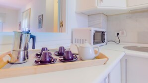 A kitchenette with a microwave, kettle, and a tray with teacups and a pitcher.