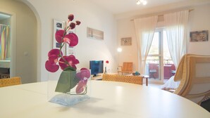 A modern living room with a white table, a clear vase with pink flowers, a television, and a comfortable seating area.