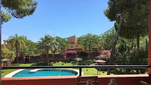 A poolside view with a wooden table and two lanterns, a clear blue sky, and a building with pink flowers in the background.