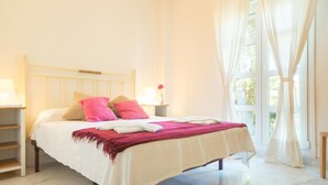 A neatly made bed with a white and pink bedspread, a wooden headboard, and a nightstand with a lamp.