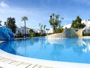 Una piscina con tobogán de agua, rodeada de palmeras y edificios blancos.