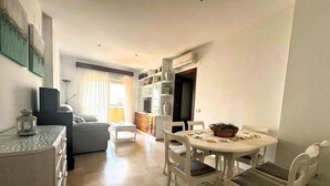 A modern living room with a sofa, a coffee table, and a dining area with a table and chairs. - Apartamento Cabo Noval 15158 (Sanlucar de Barrameda)