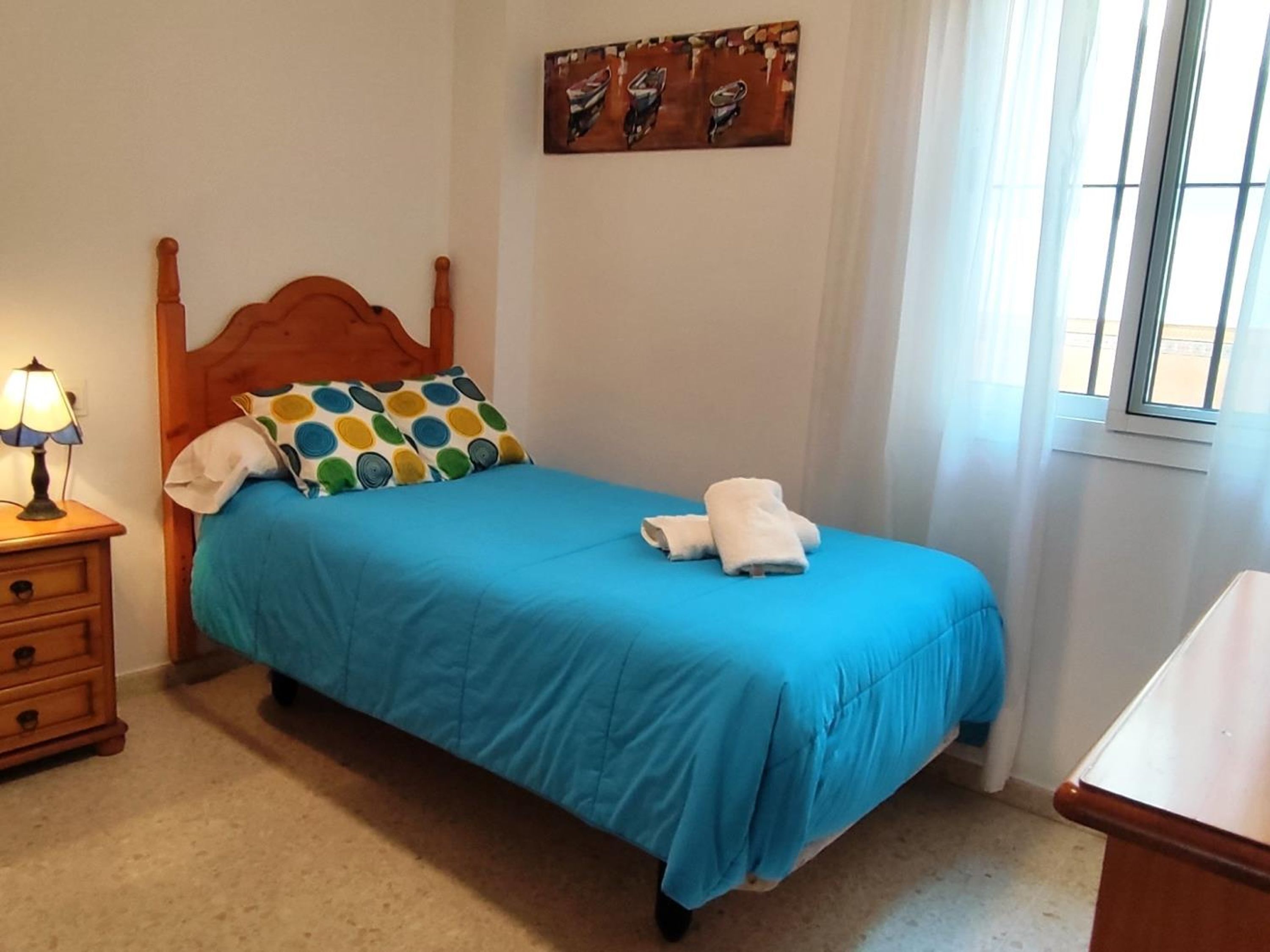 Un dormitorio con una cama de madera, una mesita de noche con una lámpara, una colcha azul y un cuadro en la pared.