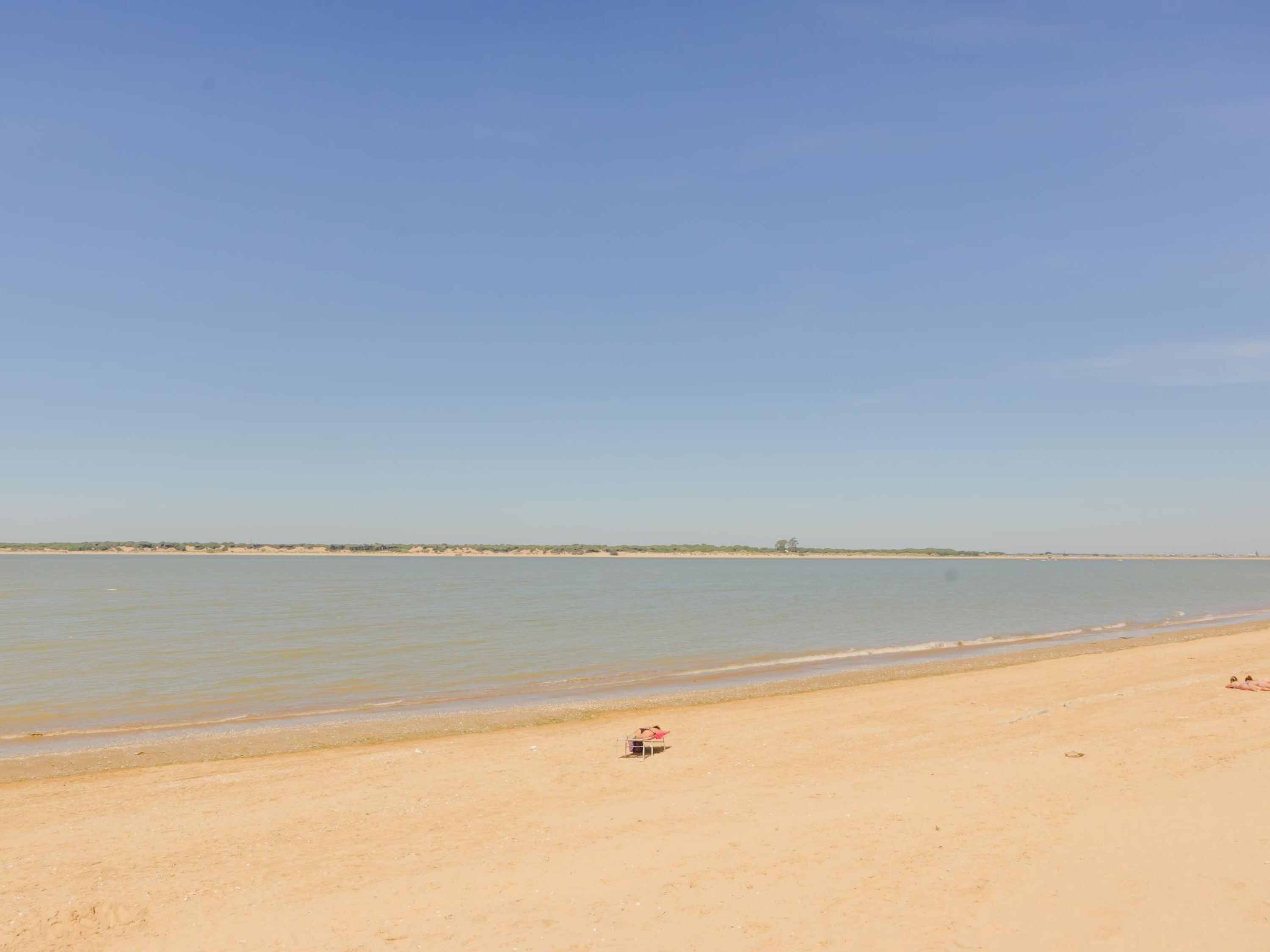 A beach with a clear sky, calm water, and a distant shoreline.