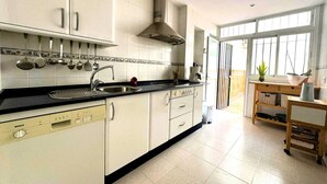 A kitchen with white cabinets, a Bosch dishwasher, a black countertop, and a window with a view of the outside. - Apartamento Cabo Noval 15158 (Sanlucar de Barrameda)