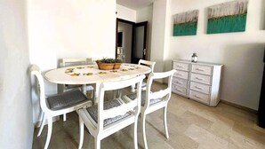 A dining area with a round table, white chairs, and a cabinet with drawers. - Apartamento Cabo Noval 15158 (Sanlucar de Barrameda)
