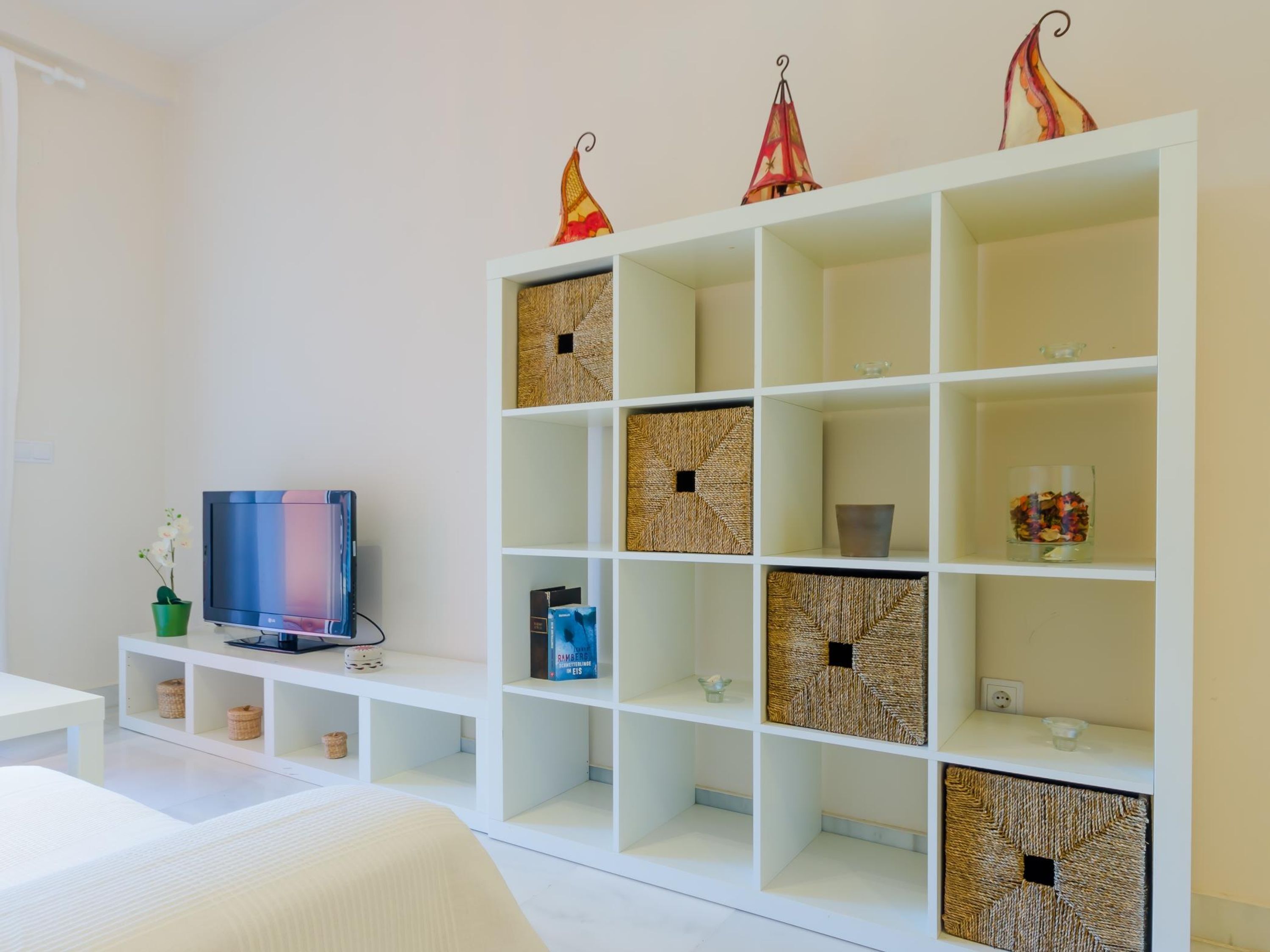A modern living room with a white TV on a stand, a white sofa, and a white shelving unit with woven baskets.