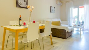 A modern living room with a dining area, a sofa, and a coffee table. There is a painting on the wall and an air conditioning unit.