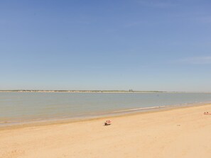 Una playa con cielo despejado, agua tranquila y una costa distante.