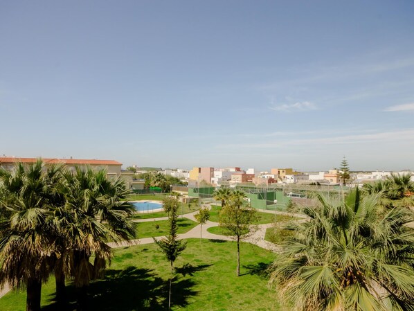 A residential area with a green lawn, palm trees, and a clear blue sky. - Apartamento Bajo de Gu a 15380 (Sanlucar de Barrameda)