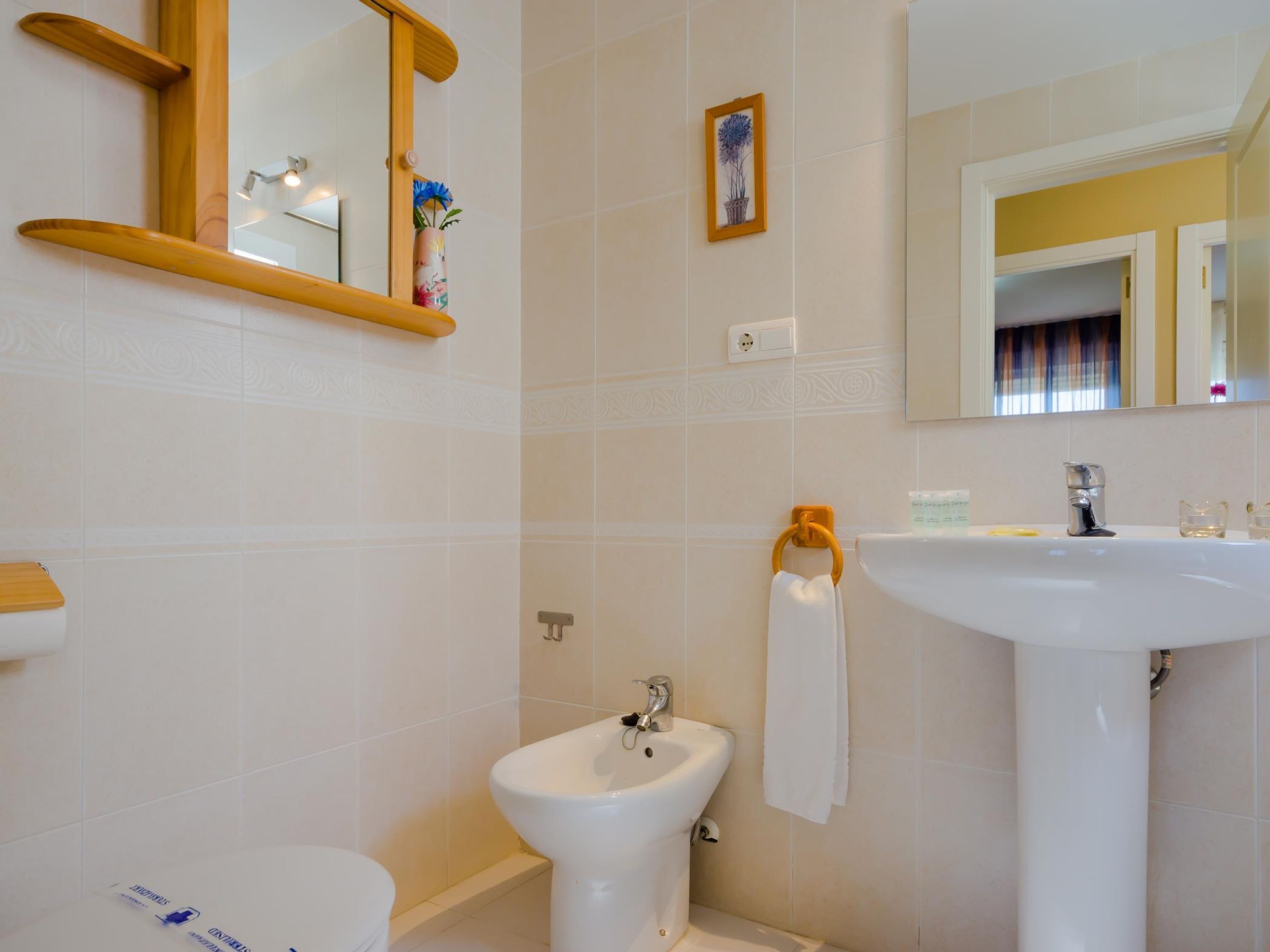 A bathroom with a toilet, bidet, and sink. There is a mirror above the sink and a framed picture on the wall.