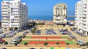 Vista de un paisaje urbano costero con edificios de varios pisos, un estacionamiento y un campo deportivo.