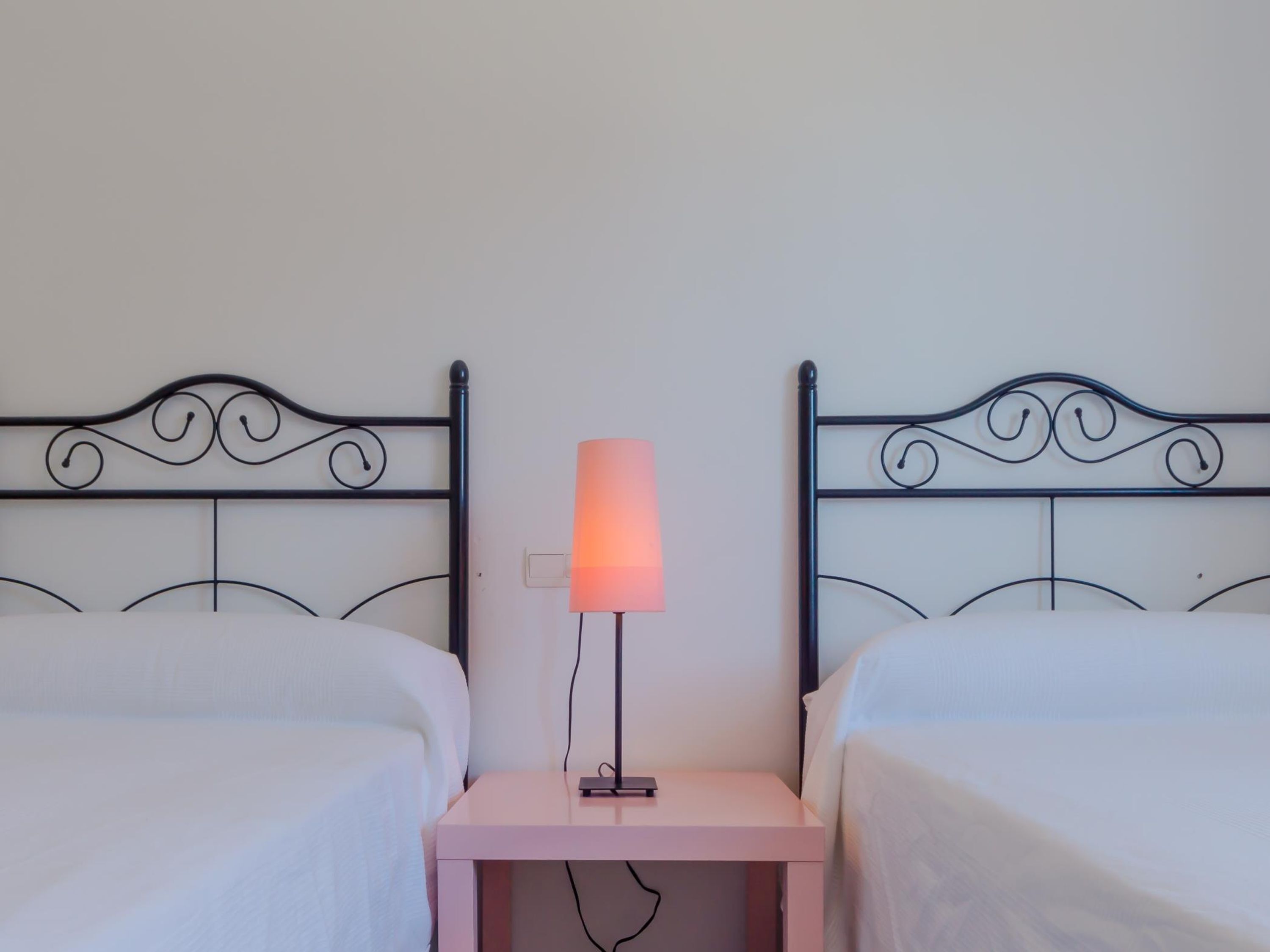 A bedroom with two beds, a nightstand, and a bedside lamp.