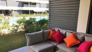 A modern outdoor seating area with a pool view, wicker furniture, and a grey cushioned sofa with colorful cushions. - Bah a Blanca II 18923 (El Puerto de Santa Maria)