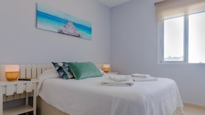 A modern bedroom with a bed, pillows, a bedside table, a lamp, and a painting on the wall. - Sea Views Rota 24397 (Rota)