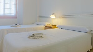 Une chambre d’hôtel avec deux lits, une table de chevet avec une lampe et une fenêtre avec des stores.