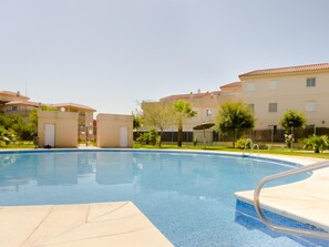 A swimming pool with clear blue water, surrounded by a well-maintained lawn and a row of buildings with a consistent architectural style.